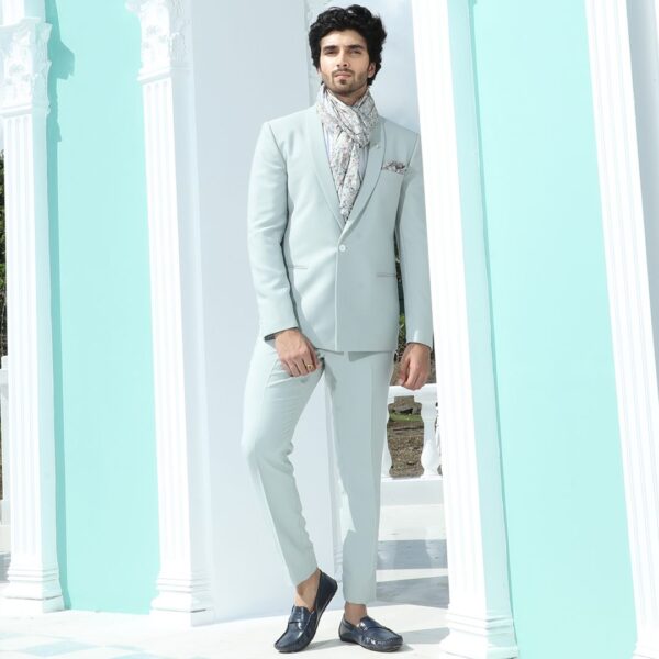 A shawl lapel powder blue blazer with single button. It is acessorised with printed  pocket square and silver crown brooch.