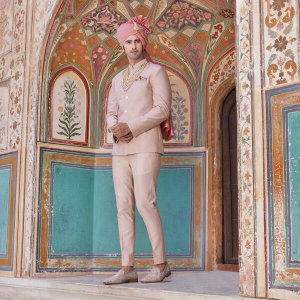 Old Rose Jodhpuri Coat with surface detailing of Forts embroidery all over. Matching trousers for bottom. Accessorised with coordinated pocket square, mala and safa in schuass pink. Styled with coordinated loafers.