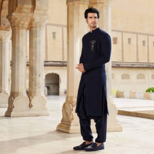 Midnight blue long asymmetric overlapped chevron textured bandhgala. Matching Afghani for bottoms. Accessorised with brooch in antique gold. Styled with coordinated loafers with crane embroidery.