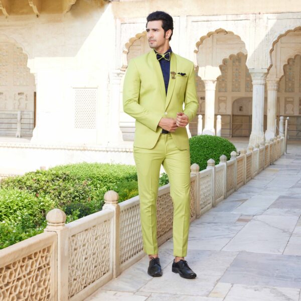 Celery green tuxedo suit with stitch line detailing on the placket paired with a midnight blue shimmer shirt. Accessorised with coordinated pocket square, brooch and bow tie. Styled with coordinated formal shoes.