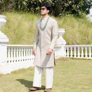 Ivory Bandhgala with hand embroidered detailing all over. Paired with coordinated flared ivory trouser. Accessorised with emerald mala.